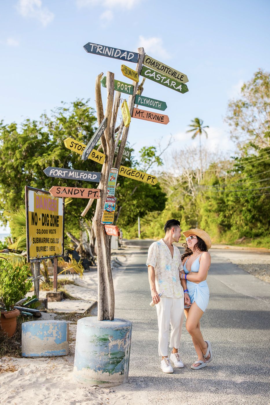 Couple poses by directional signs and barrels in a tropical location.