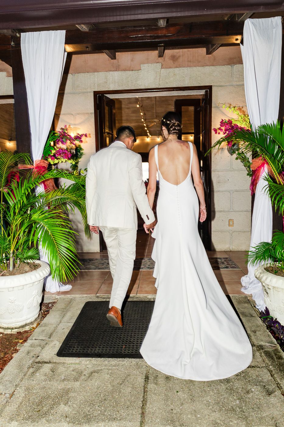 Guests in formal attire entering venue through white curtained doorway.