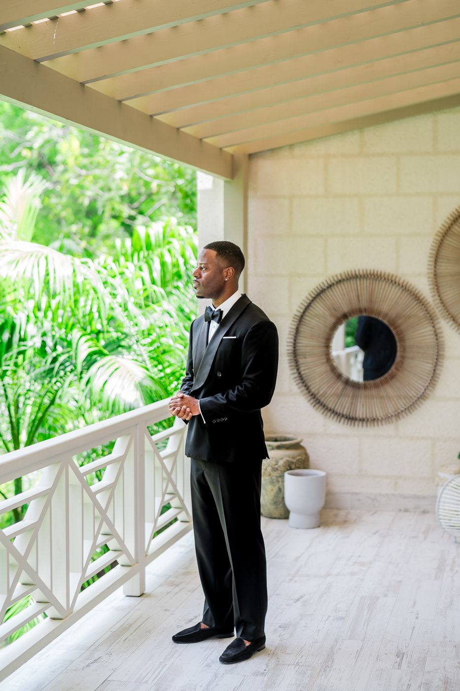 A covered porch with white railings features circular mirror decor and tropical garden views.