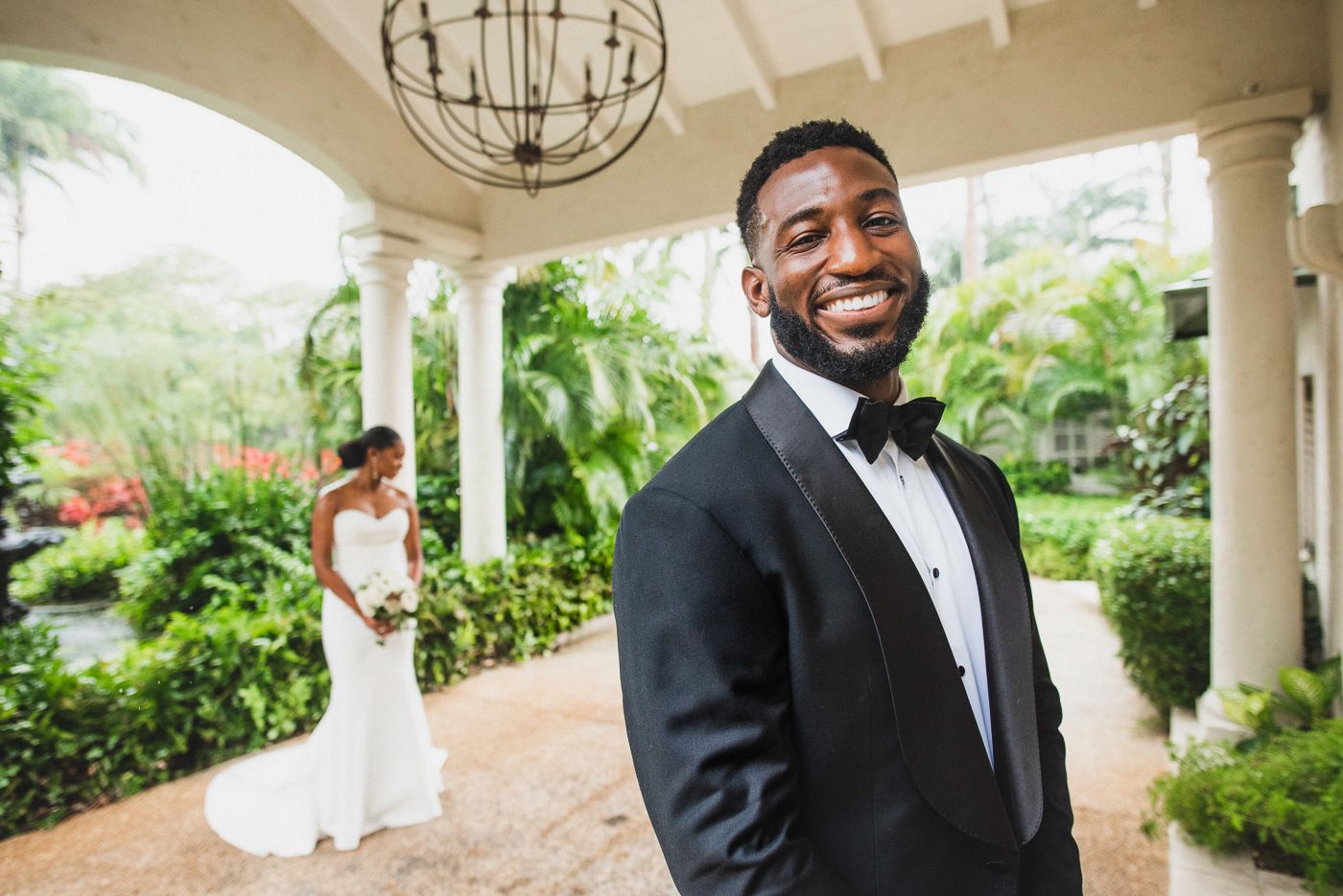 Classic wedding portrait in tropical garden setting with white pillared architecture.