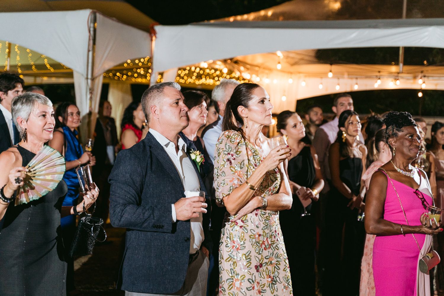 Wedding reception guests dance and celebrate under outdoor tent in evening atmosphere.