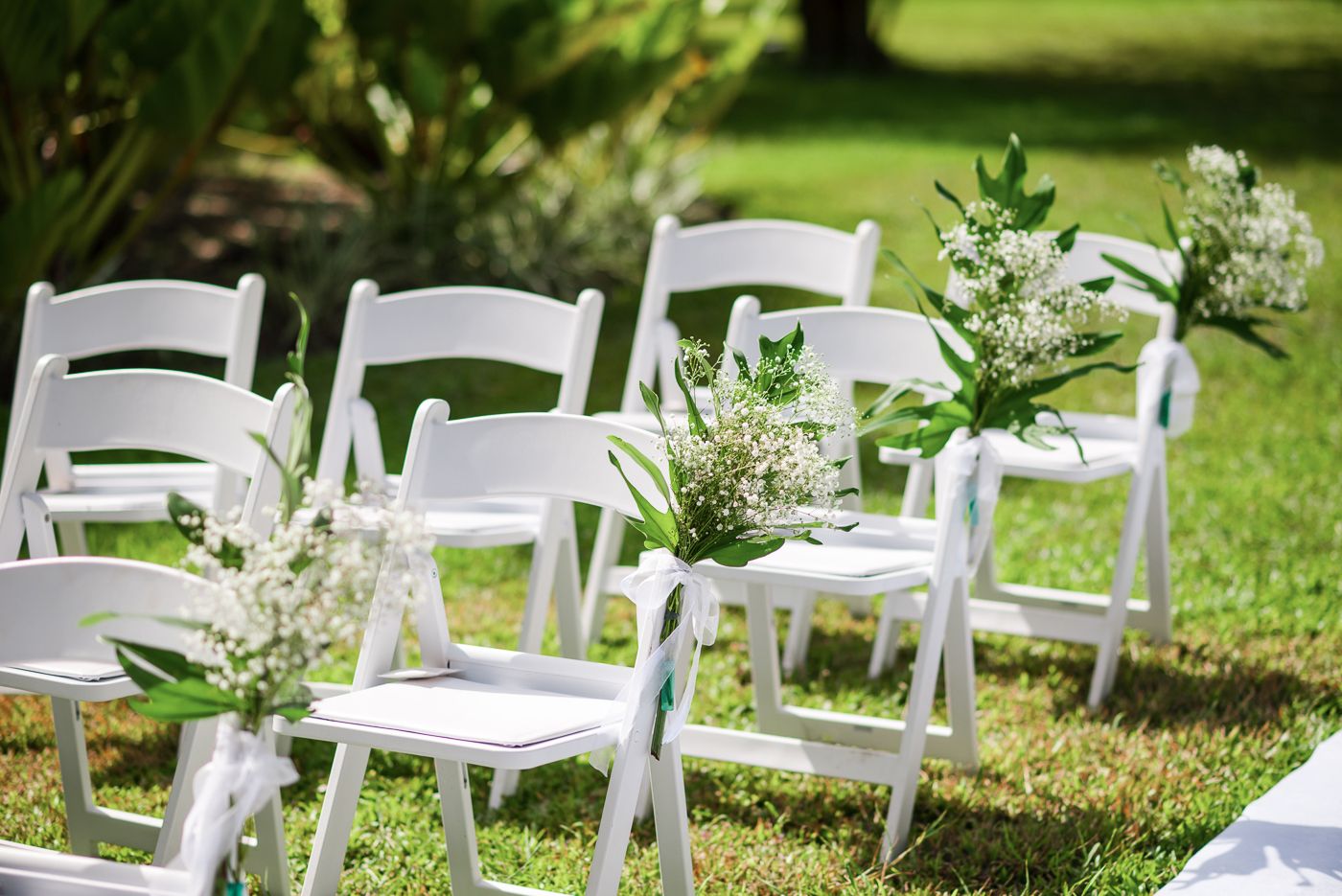 White folding chairs decorated with delicate white flowers set up for outdoor garden ceremony.