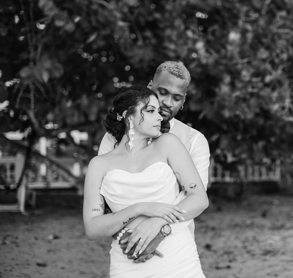 Black and white wedding photo of a couple embracing outdoors, groom holding bride in white strapless gown.