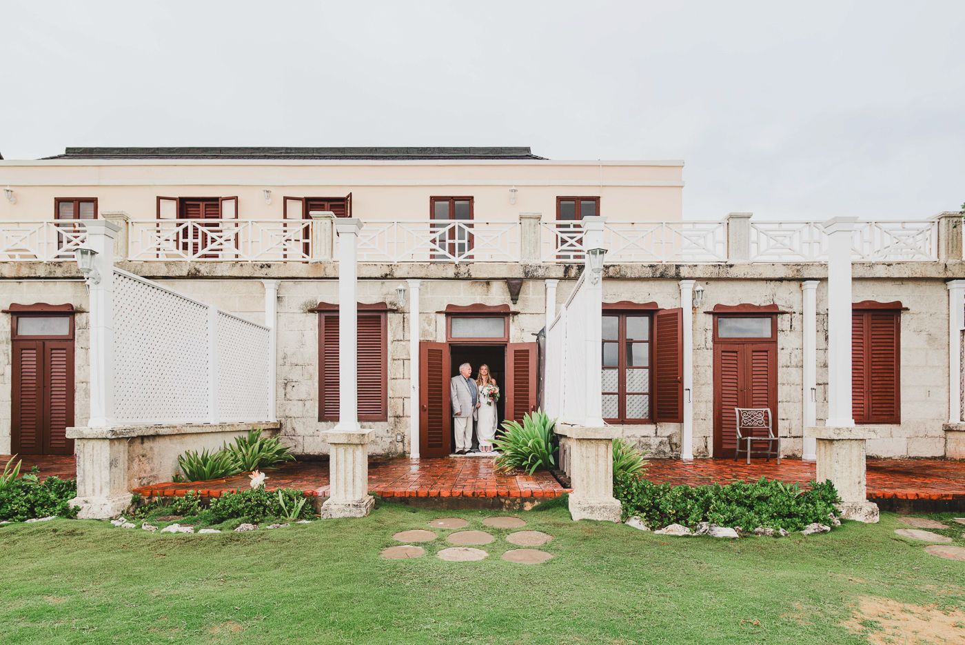 Couple standing in doorway of elegant colonial-style building with white columns and manicured lawn.