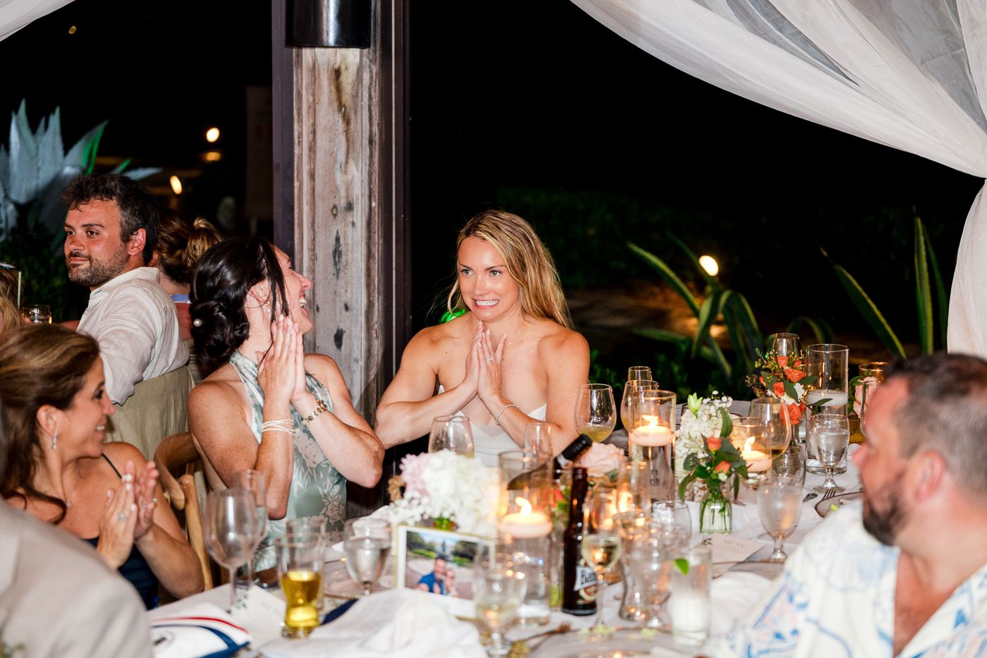 Guests clapping and celebrating at an elegant outdoor wedding reception dinner with candlelit tables.