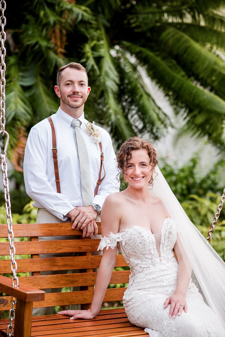 Couple shares romantic moment on wooden swing surrounded by tropical foliage.