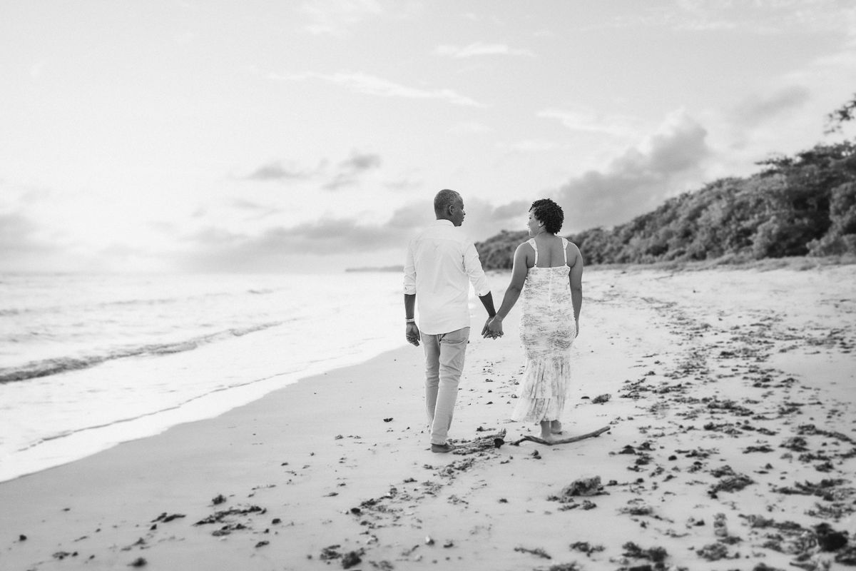 People in white outfits walk along a scenic beach shoreline during a cloudy day.