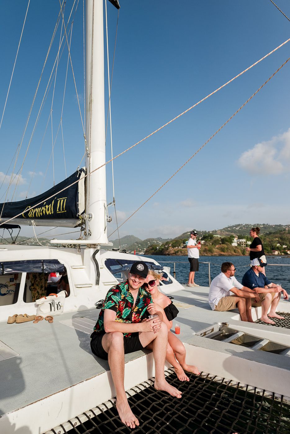 Group relaxing on the deck of a white catamaran sailing boat in tropical waters.