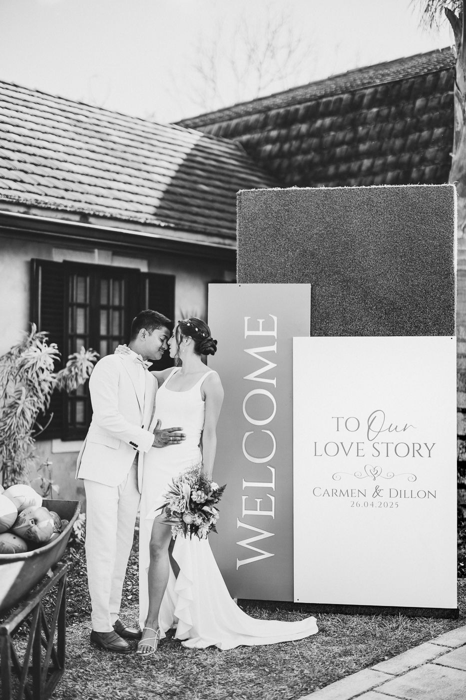 Black and white wedding welcome sign display with couple in background.