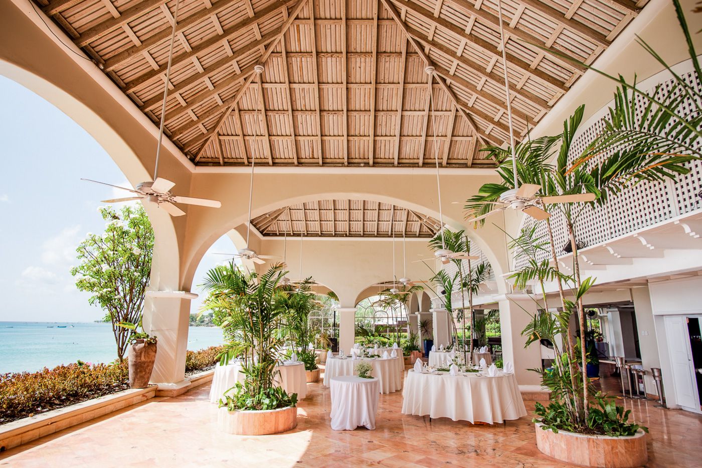 Covered outdoor tropical reception venue with wooden beamed ceiling and white drapery.