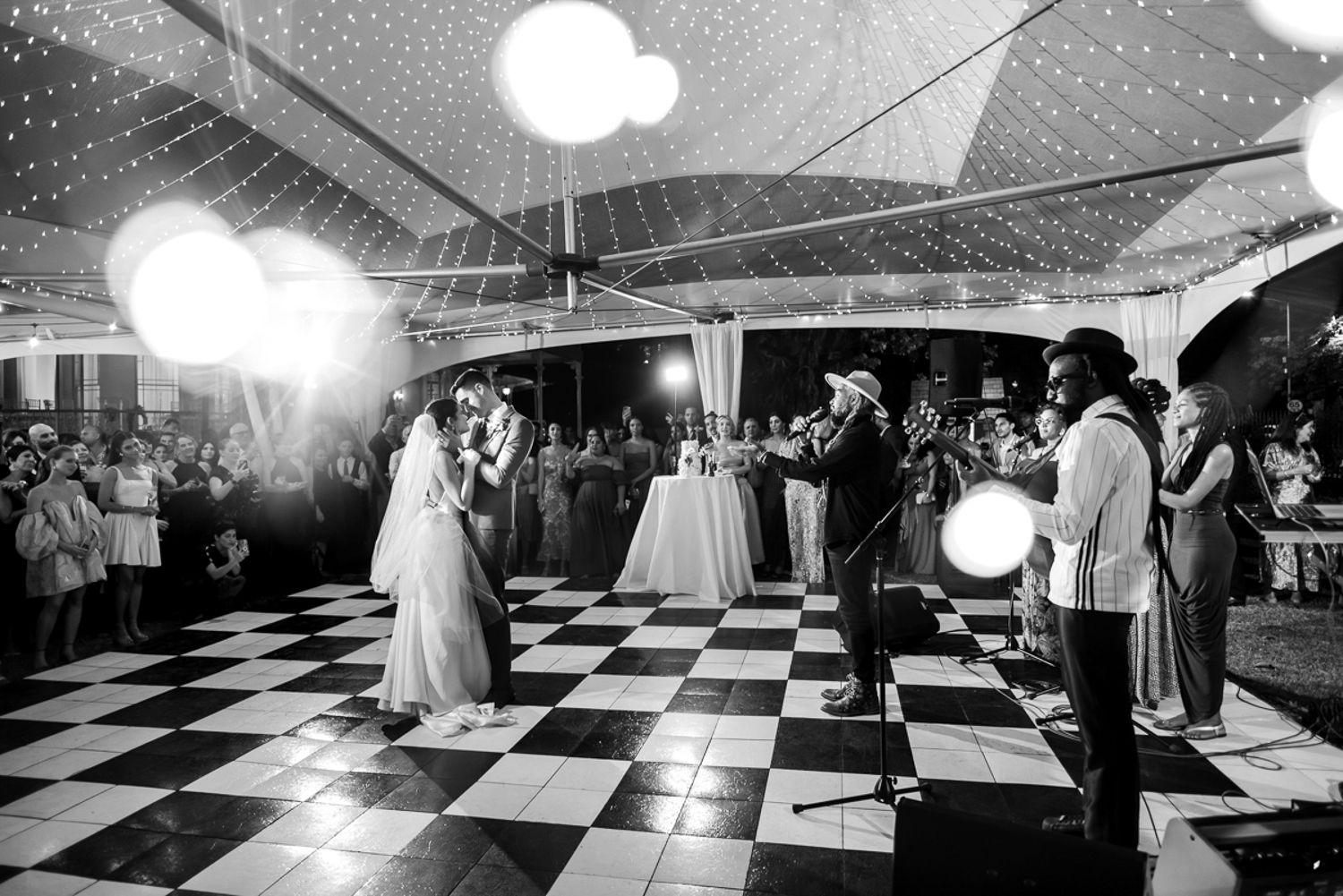 A black and white checkered dance floor at a wedding reception with people dancing under ambient lighting.