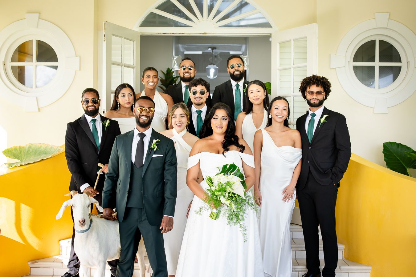 Wedding party members gather in a white hallway with arched windows and yellow walls.