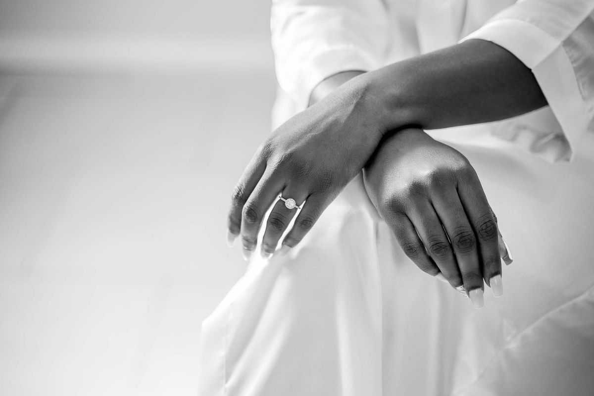 Black and white photo of a woman's hands wearing a diamond engagement ring, draped in white fabric.