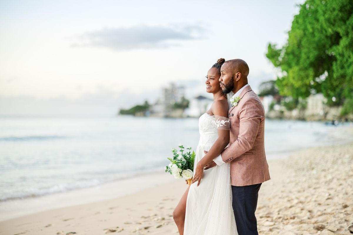 A couple shares an intimate moment on a tropical beach with palm trees and ocean waves in the background.
