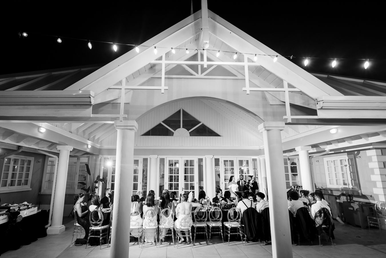 Wedding reception gathering under an illuminated white pavilion during evening celebrations.