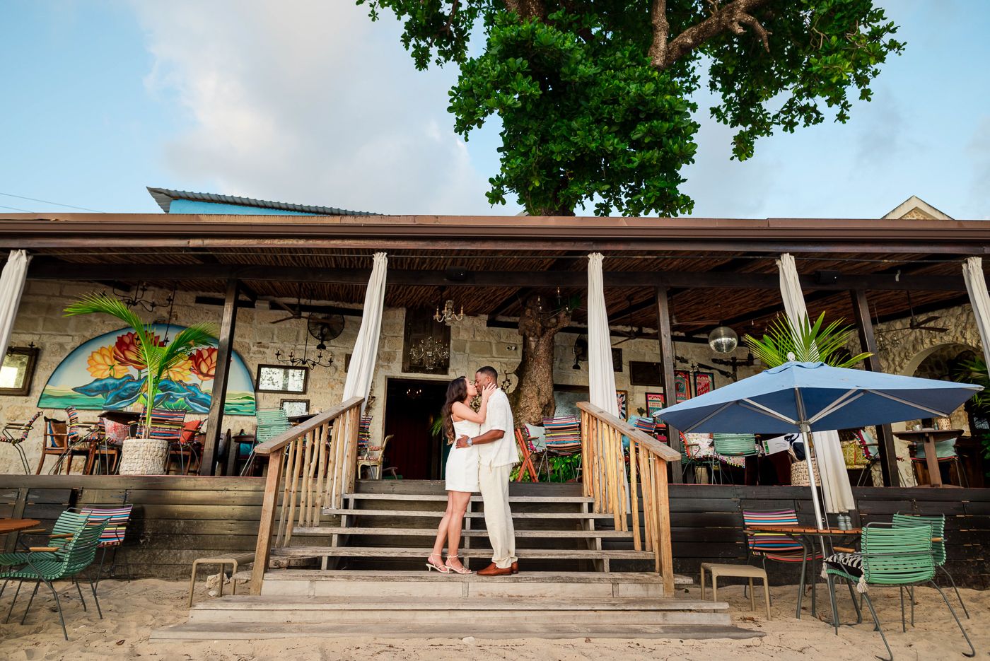 A couple embraces on the steps of a beachfront restaurant at sunset, in Speightstown, Saint Peter Barbados