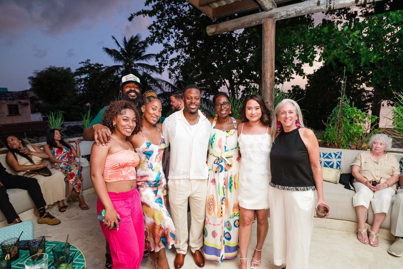 A festive group of people gathered at an outdoor party venue at dusk wearing summer attire.
