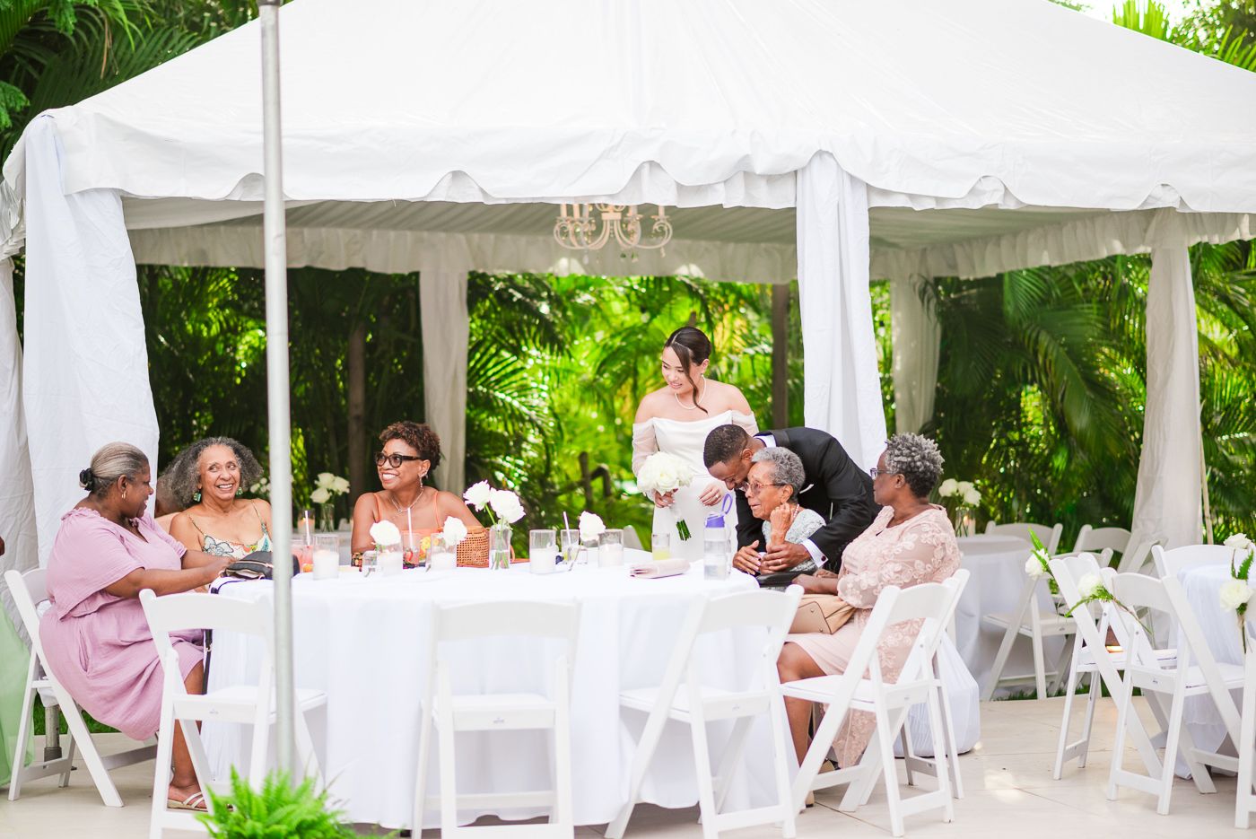 Wedding guests gathered at round tables under a white tent for an outdoor reception.