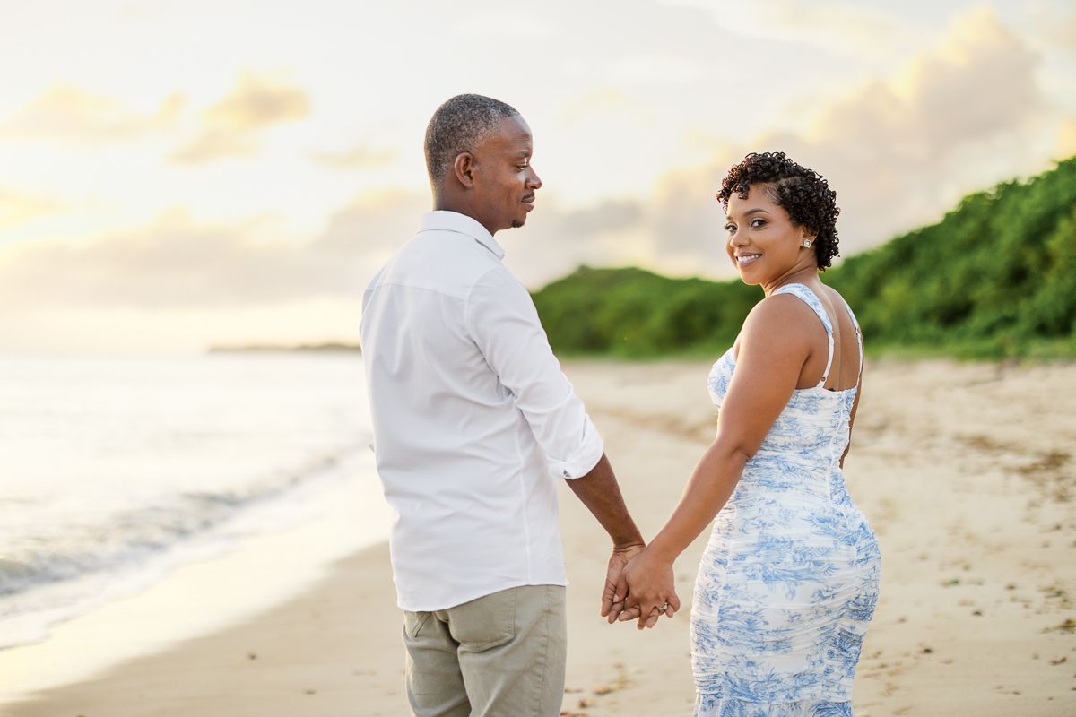 A couple in white and blue outfits shares romantic moments during a beach photo session at sunset.