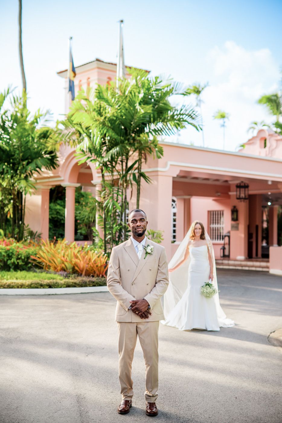 Wedding photos taken outside pink Spanish colonial building entrance with palm trees.