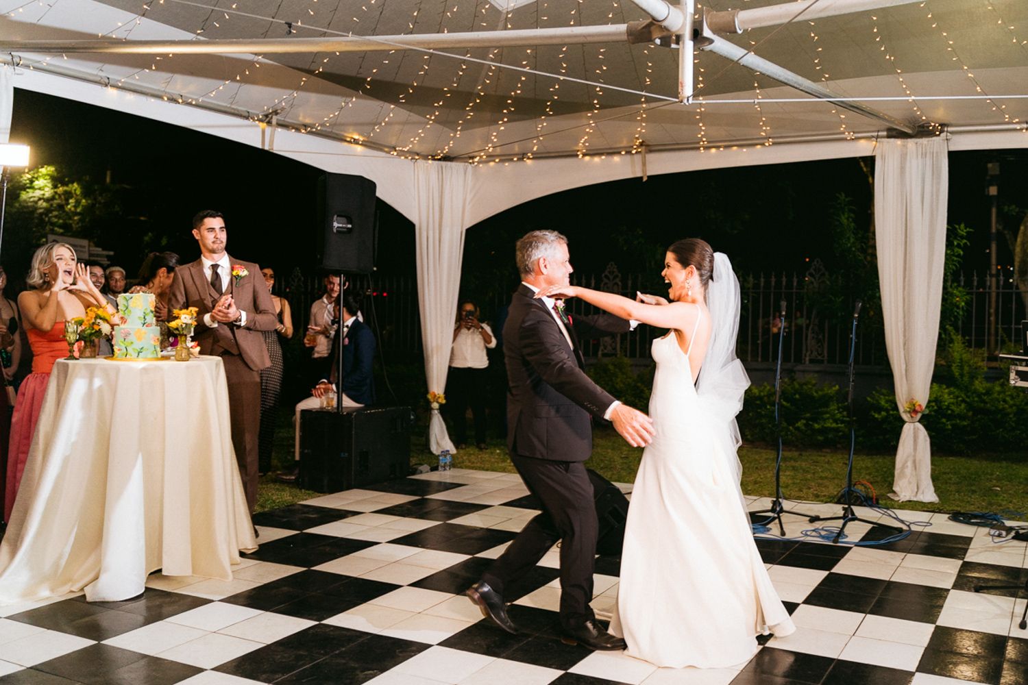 A black and white checkered dance floor hosts elegant wedding reception dancing under a white tent.