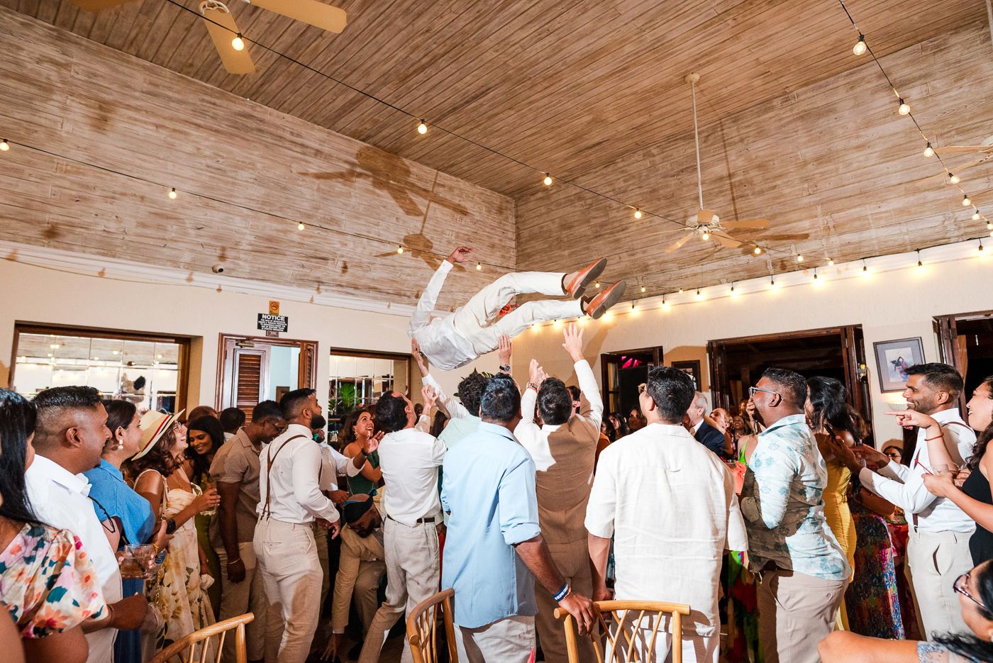 Panoramic view of wedding reception showing guests dancing under rustic wooden ceiling.