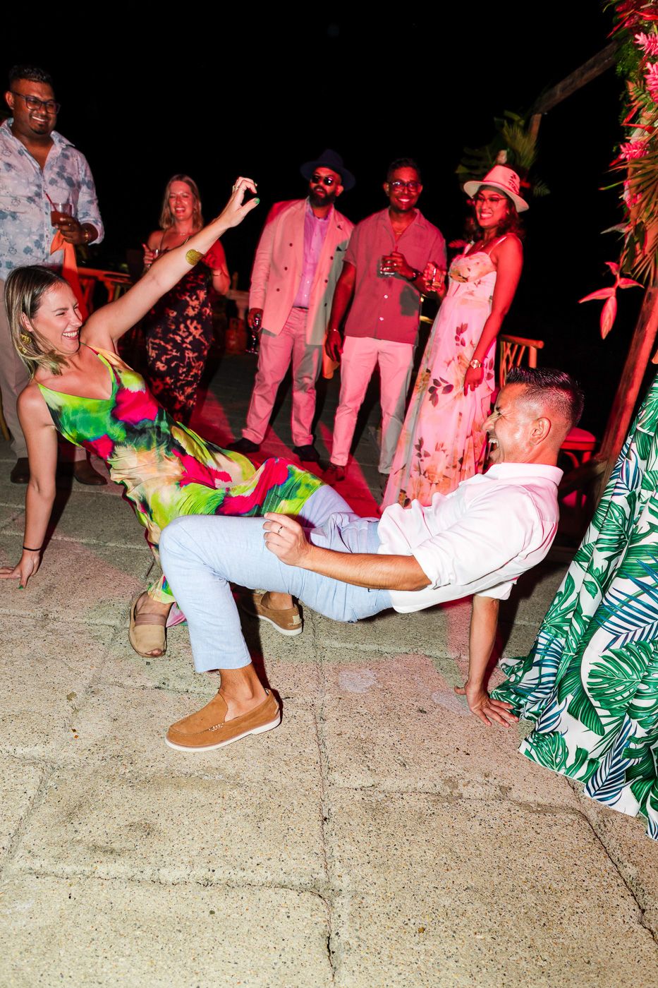 Party guests performing limbo dance moves at a tropical themed outdoor celebration.