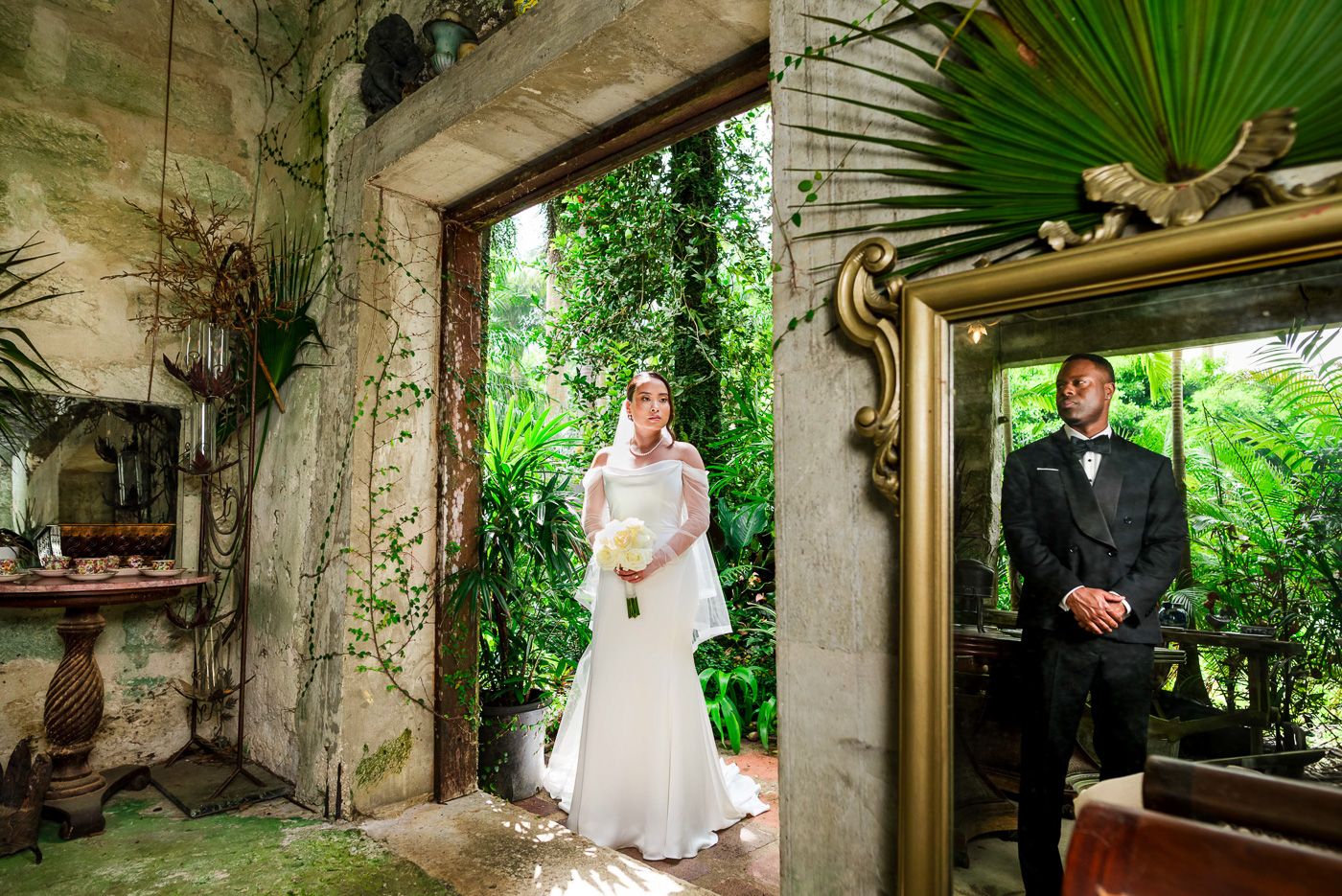 Wedding portrait in rustic stone archway with tropical garden backdrop.