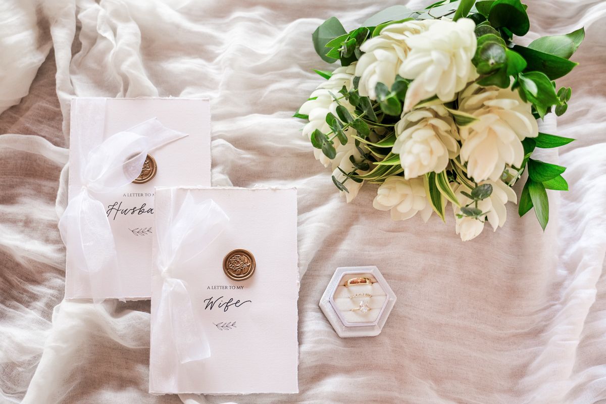 Wedding invitation cards and white floral bouquet arranged on soft linen fabric with hexagonal ring box.