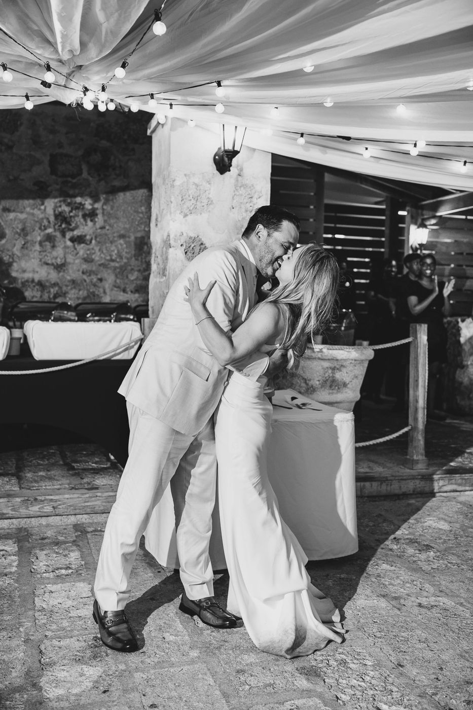 Black and white photo of bride and groom sharing first dance kiss at outdoor wedding reception.