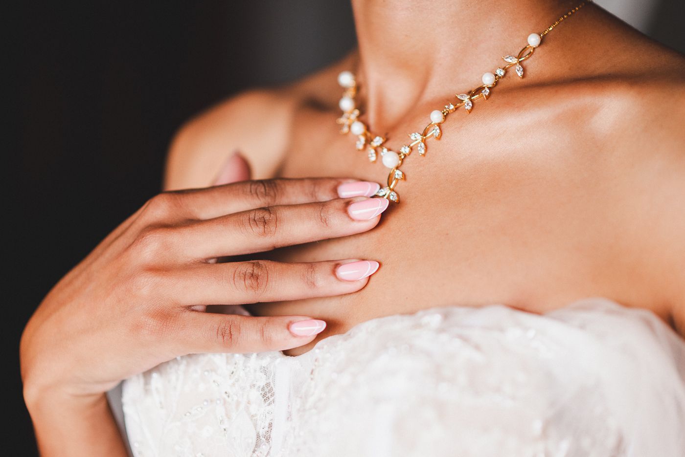Close-up view of hands wearing pink nail polish and delicate jewelry resting on white lace fabric.