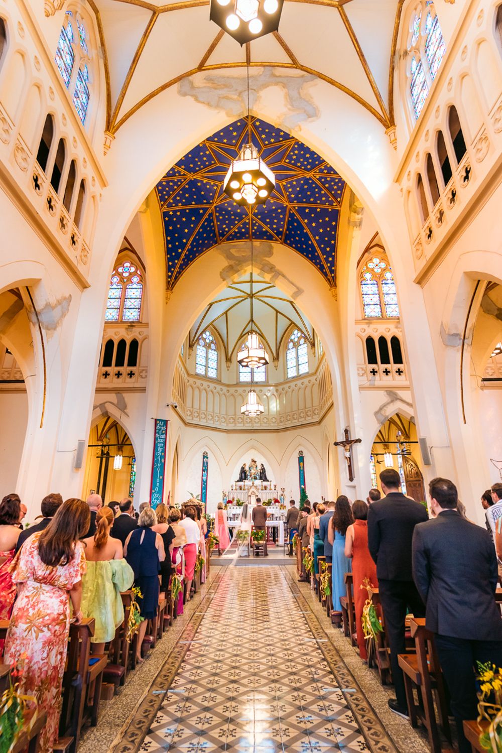 Gothic church interior with vaulted ceilings and blue stained glass windows filled with wedding guests.
