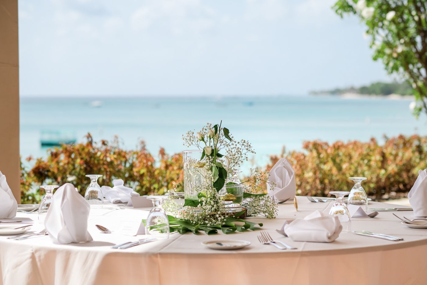 Elegant wedding table setting with white linens and tropical floral centerpiece overlooking the ocean.
