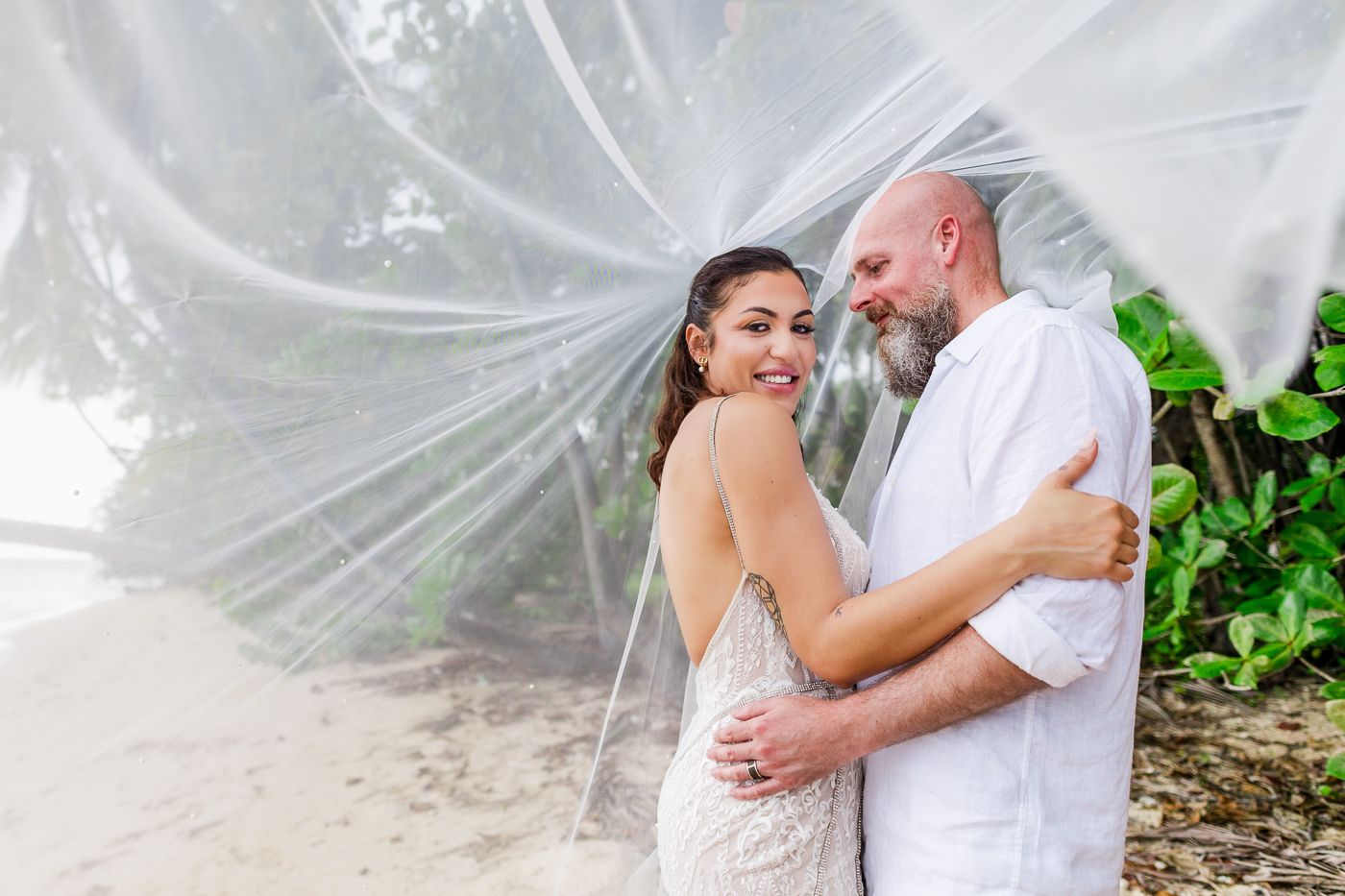 A romantic wedding photo with flowing white veil in a dreamy tropical garden setting.