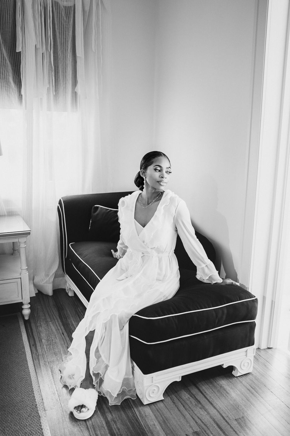 Black and white portrait of person in flowing white dress reclining on velvet sofa.