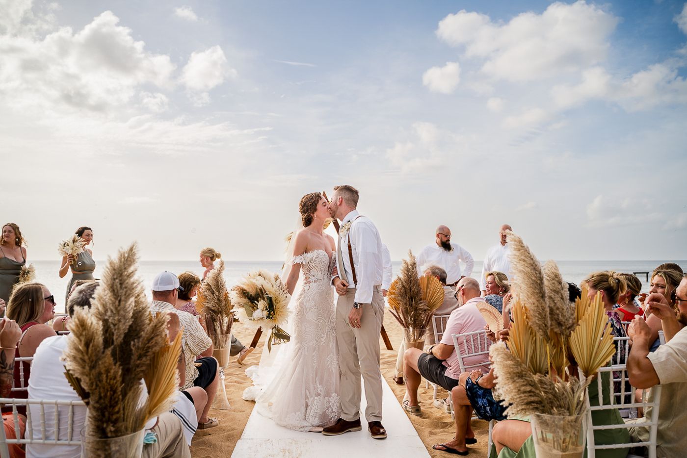 Wedding ceremony guests celebrating at a beachside venue with pampas grass decorations.