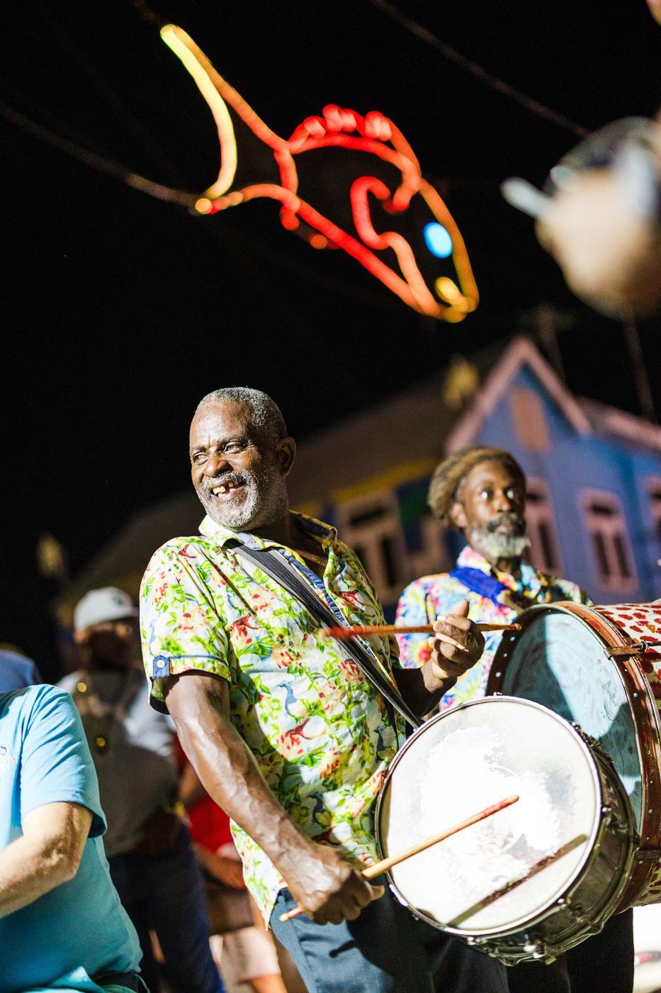 Musicians performing with drums under colorful neon fish decorations at night.