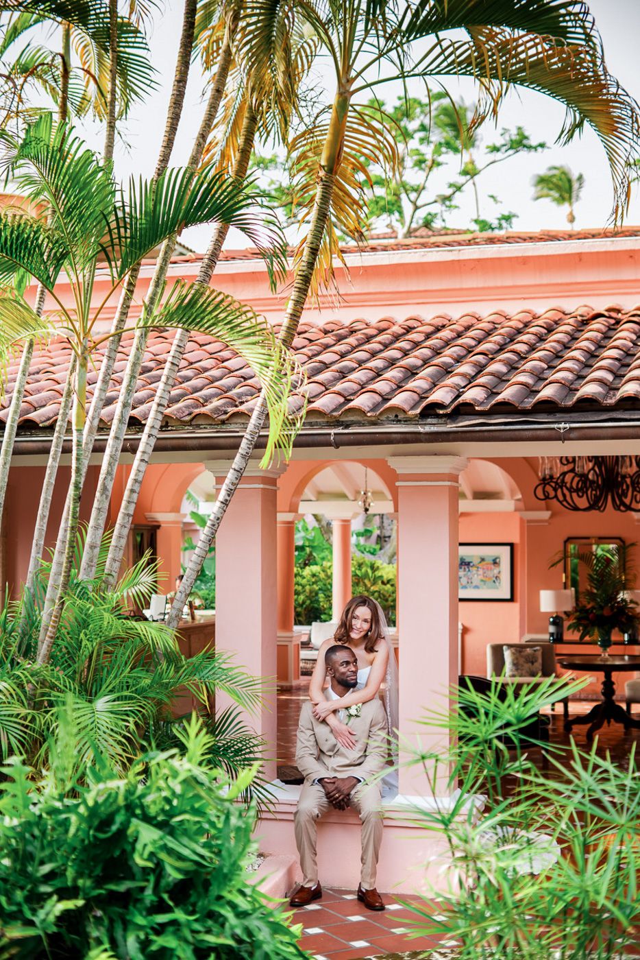 Palm-lined courtyard with pink Spanish colonial architecture and wedding portraits.