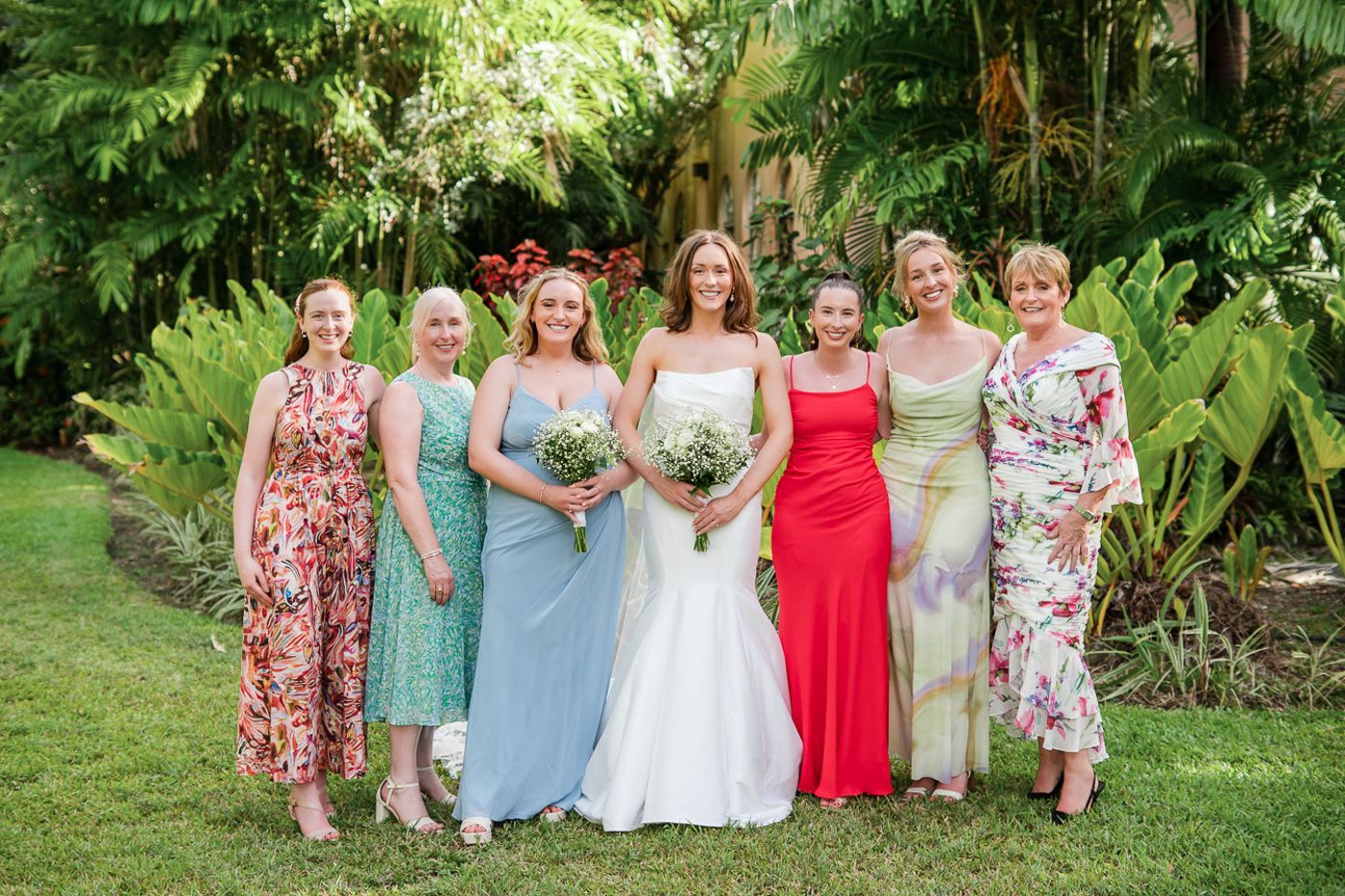 Wedding party in colorful floral dresses and pastels posing in a tropical garden setting.