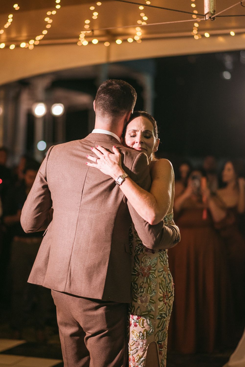 Two people share an intimate slow dance at an evening reception under warm string lights.