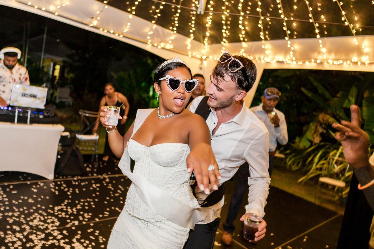 Wedding couple dances under romantic string lights at an outdoor evening reception celebration.