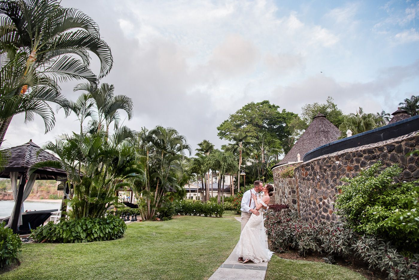 Tropical garden wedding setting with palm trees and stone wall pathway.