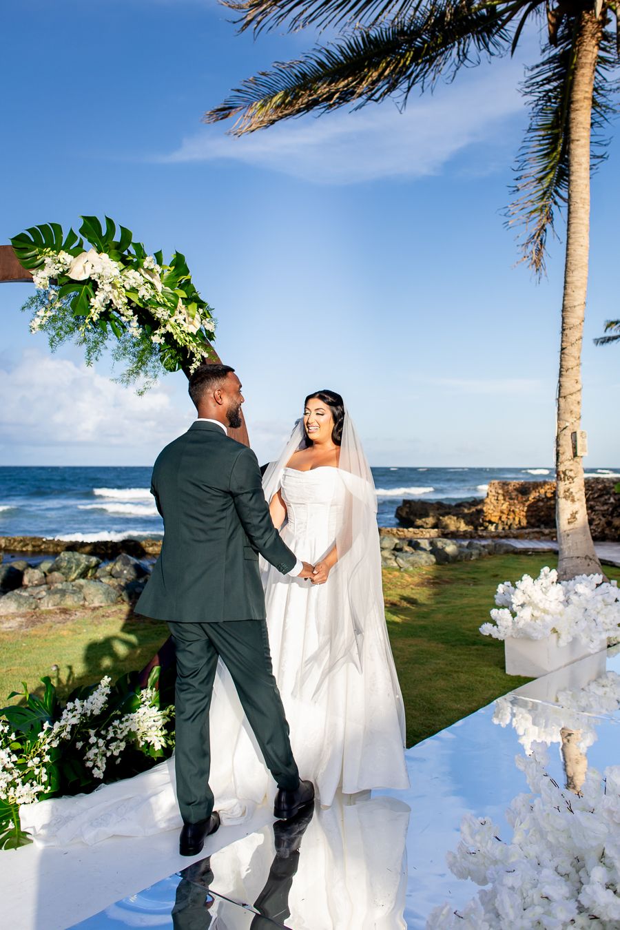 Beachside wedding ceremony with white floral decorations and swaying palm trees.