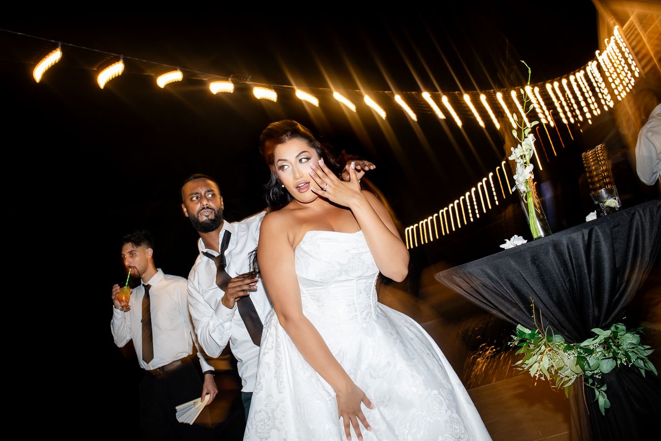 Wedding party dancing in a line under illuminated string lights at night.