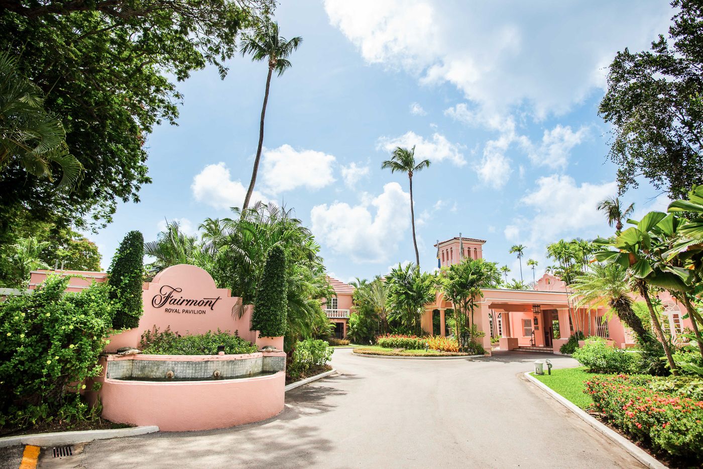 Pink Mediterranean-style resort entrance with palm trees and tropical landscaping along a curved driveway.