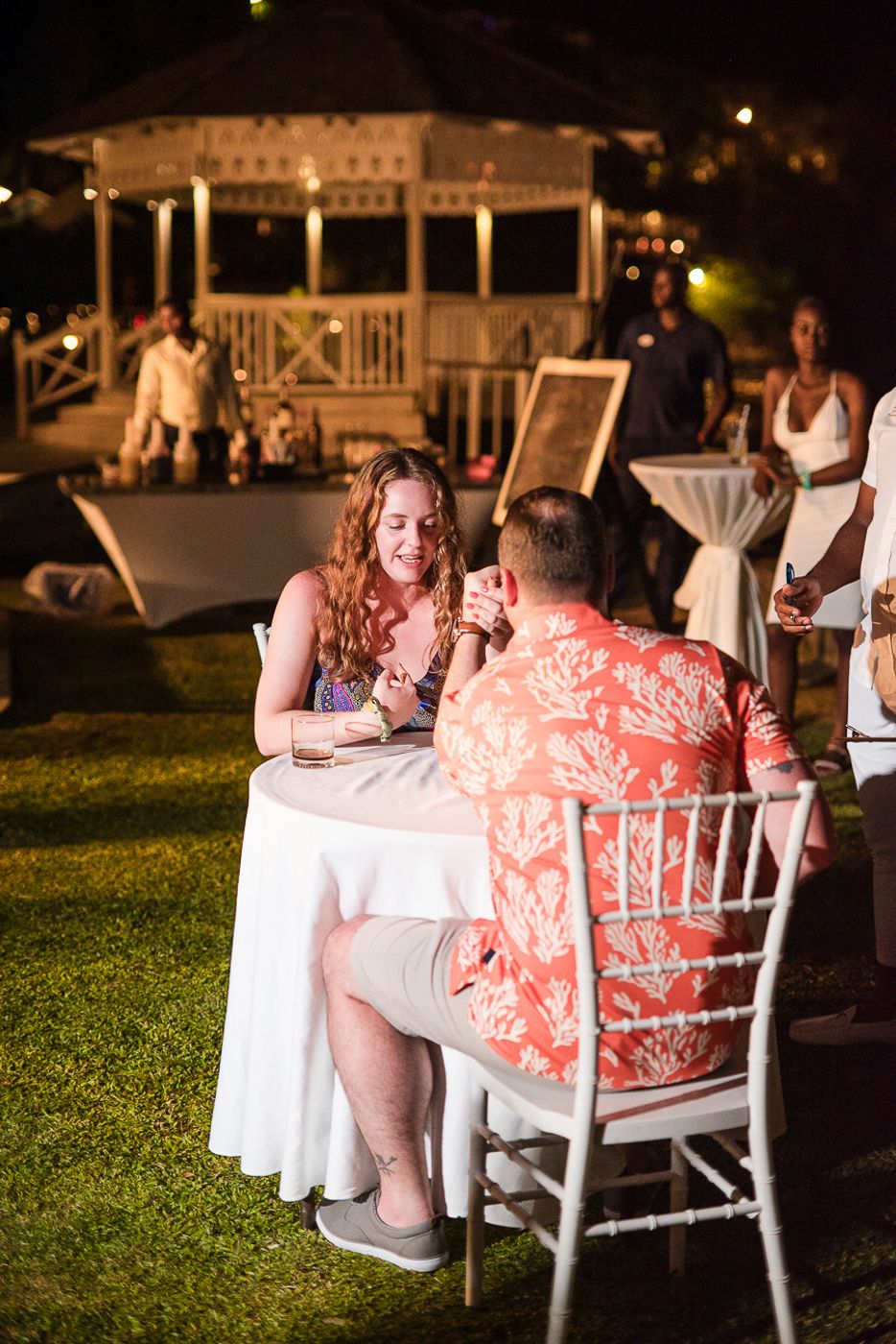 Couple sitting at a round table near a gazebo during an evening outdoor event.