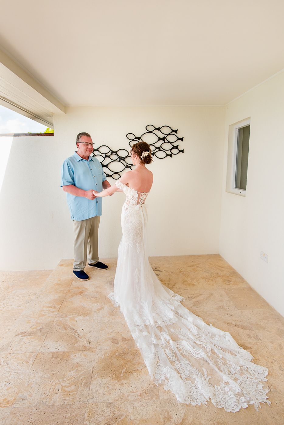 Wedding dress with long lace train trails behind during a special moment in a minimalist room.