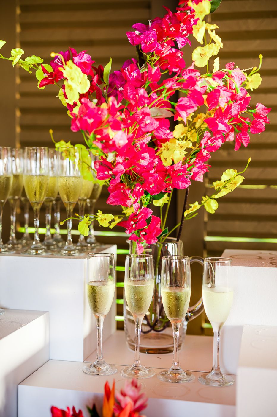 Vibrant pink and yellow orchid centerpiece with champagne flutes on white tablecloth.