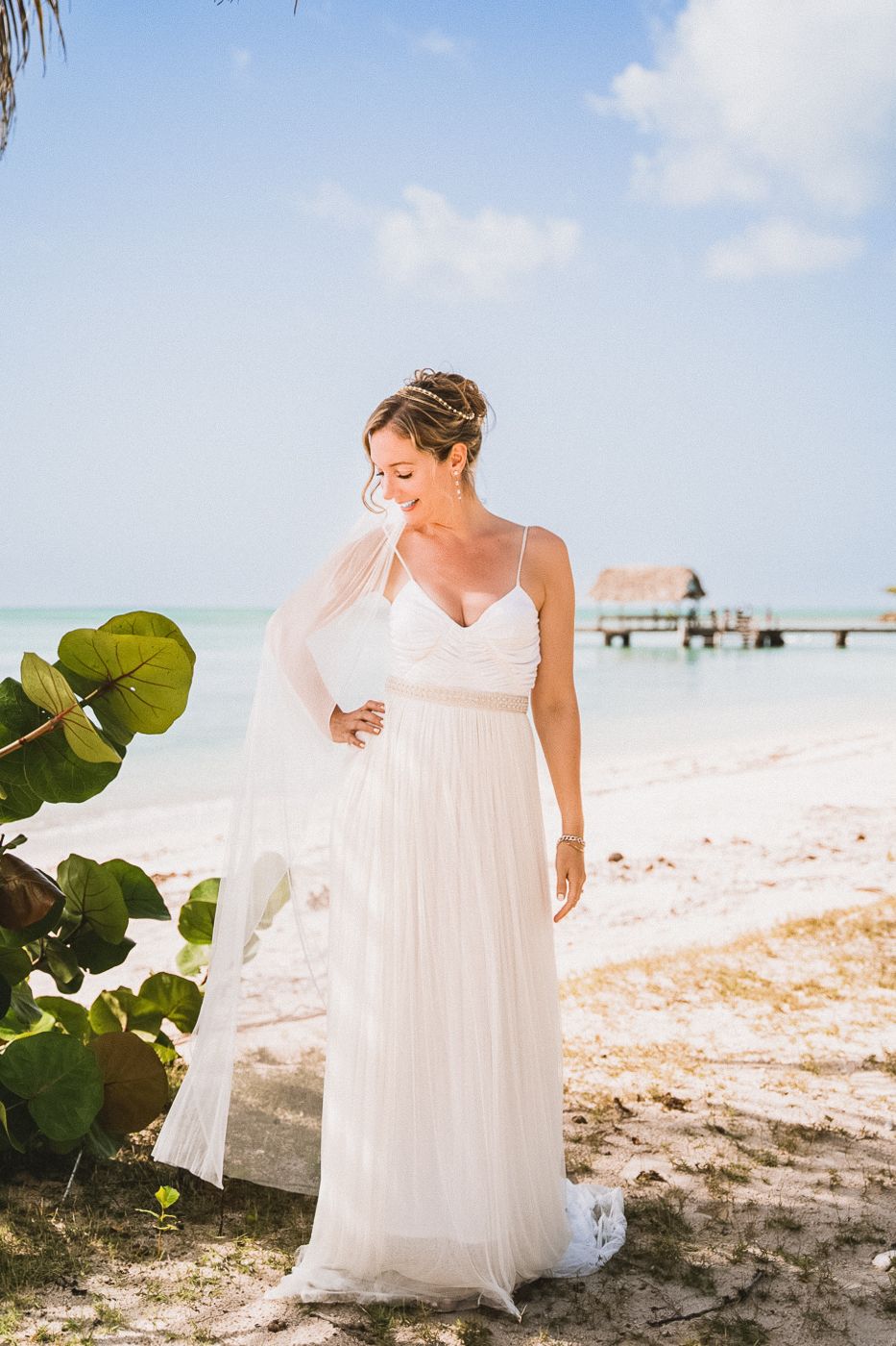 Flowing white wedding dress captured in beach setting with tropical foliage.
