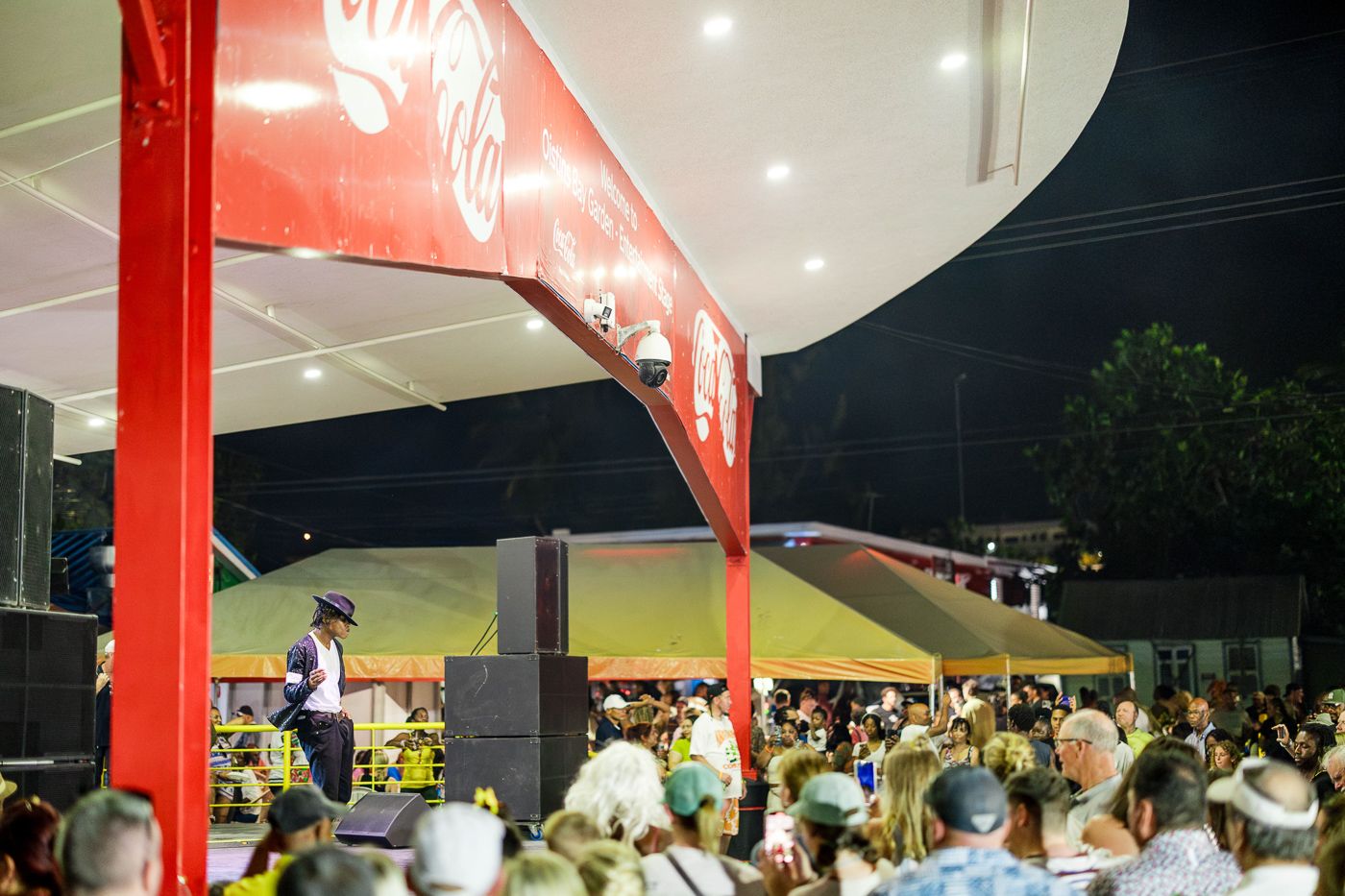 Nighttime crowd gathered under red outdoor venue signage with bright lighting.